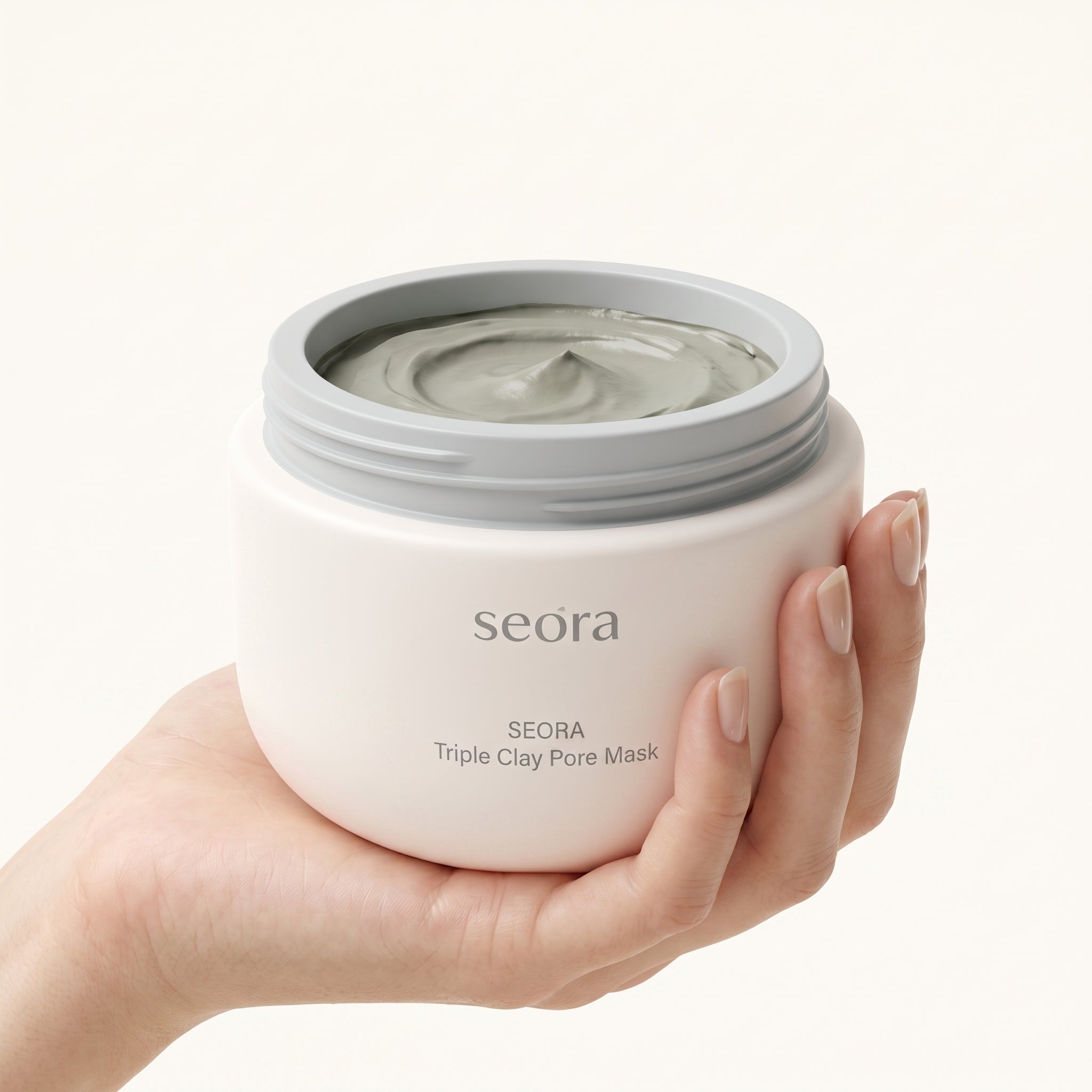 A hand holding an open jar of Seora Triple Clay Pore Mask, showing the gray clay mask inside against a clean, off-white background.
